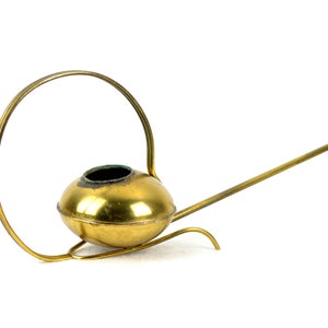 May include: A gold-colored metal watering can with a long spout and a circular handle. The watering can has a round, bulbous body.