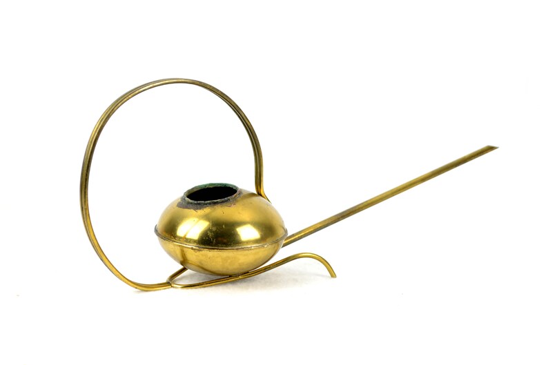 May include: A gold-colored metal watering can with a long spout and a circular handle. The watering can has a round, bulbous body.