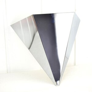 May include: A shiny, silver, triangular-shaped wall vase with a pointed bottom.