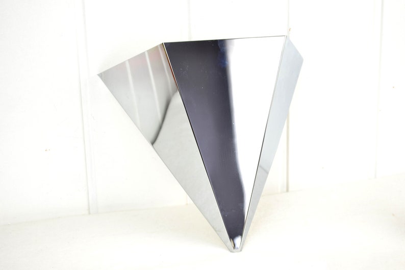 May include: A shiny, silver, triangular-shaped wall vase with a pointed bottom.