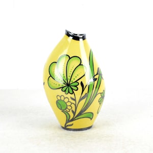 May include: A yellow ceramic vase with a unique, asymmetrical shape. It features a floral design with green and black accents.