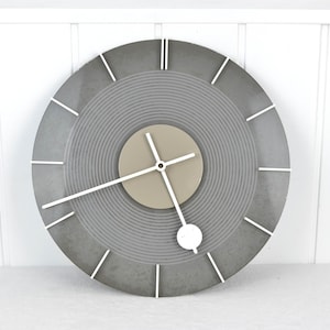 May include: A gray and white circular wall clock with a concentric circle design. The clock has white hands and a white second hand.