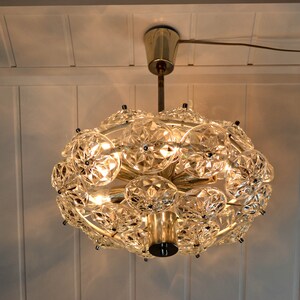 Op de afbeelding: Een ronde gouden en kristallen kroonluchter met meerdere heldere kristallen facetten. De kroonluchter heeft een modern ontwerp en wordt verlicht met warm wit licht.