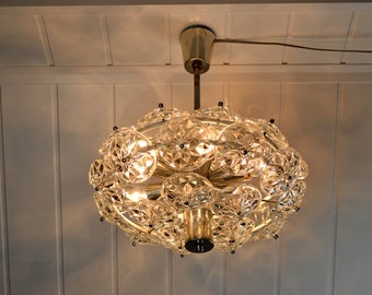 May include: A gold and crystal chandelier with a round shape and multiple clear crystal facets. The chandelier has a modern design and is lit with warm white light.