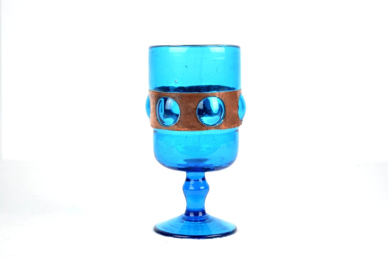 May include: A blue glass goblet with a copper band and circular accents around the middle.