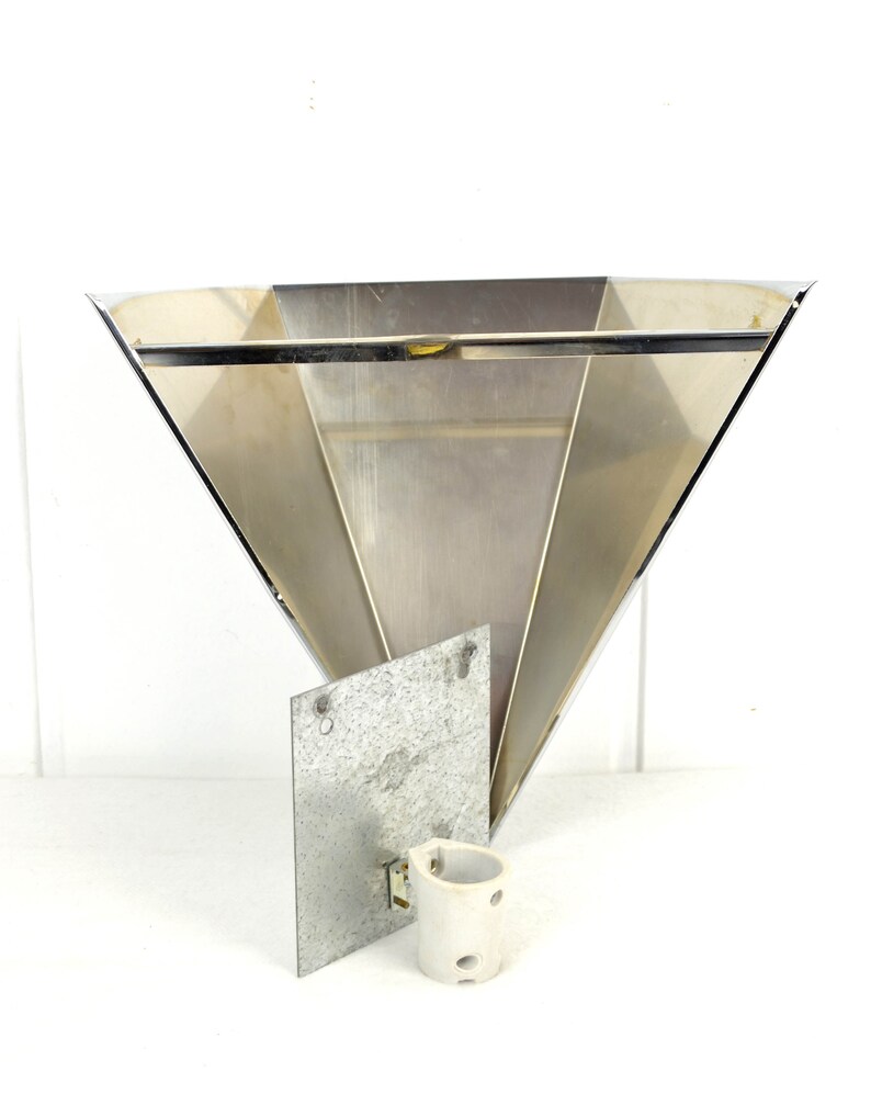 May include: A silver metal wall sconce with a triangular shape and a flat back plate. The sconce has a simple design and is made of polished metal.