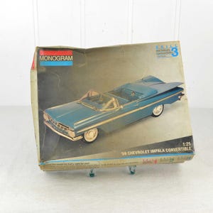 Könnte beinhalten: Vintage Modellbausatz-Box mit einem tealfarbenen '59 Chevrolet Impala Cabrio. Die Box hat das Monogram-Logo und den Text "Skill Level 3". Das Modell ist im Maßstab 1:25.