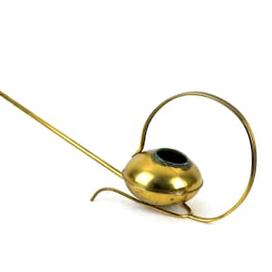 May include: A gold-colored watering can with a long spout and a circular handle. The watering can is made of metal and has a shiny finish.