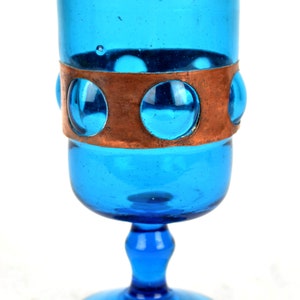May include: A blue glass goblet with a copper band and circular cutouts. The goblet has a wide base and a tall, slender stem.