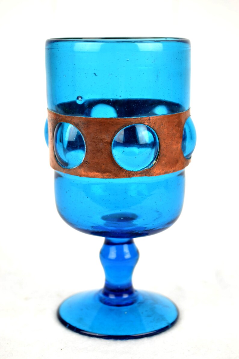 May include: A blue glass goblet with a copper band and circular cutouts. The goblet has a wide base and a tall, slender stem.