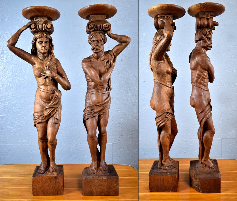 Puede incluir: Dos esculturas antiguas de madera de un hombre y una mujer, cada una de pie sobre un pedestal con una parte superior redonda. Las esculturas est&aacute;n talladas en un estilo realista y presentan detalles intrincados.