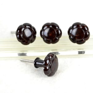 May include: Four dark brown, round, decorative cabinet knobs with a raised, flower-like design. The knobs have a silver screw in the back.