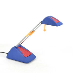 Könnte beinhalten: Eine blaue Schreibtischlampe mit einem roten und orangefarbenen Akzent. Die Lampe hat einen flexiblen Arm und einen Sockel mit dreieckiger Form.