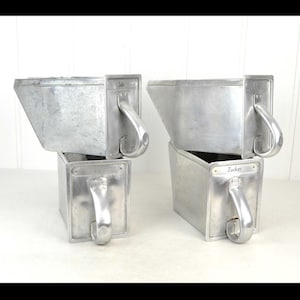 Peut inclure: Quatre récipients métalliques vintage avec des poignées. Les récipients sont rectangulaires avec un dessus incliné et une poignée incurvée. Le métal a une finition argentée brossée. Un récipient porte le mot "Zucker".
