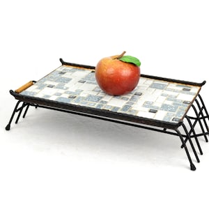 Puede incluir: Una bandeja de metal negro con una parte superior de mosaico. La bandeja tiene un asa de madera y está sostenida por cuatro patas. Una manzana roja se encuentra sobre la bandeja.