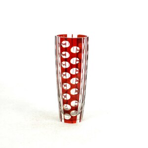 May include: A tall, red glass vase with a pattern of white circles. The vase is approximately 8 inches tall and has a cylindrical shape. The red color is vibrant, and the white circles are evenly spaced.