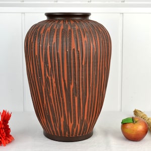 May include: A large, brown and orange ceramic vase with a textured, wood-grain design. The vase is sitting on a white surface.