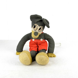 May include: A vintage plush toy of Mickey Mouse, wearing a black hat and red overalls. The toy has large, black eyes and a brown nose.