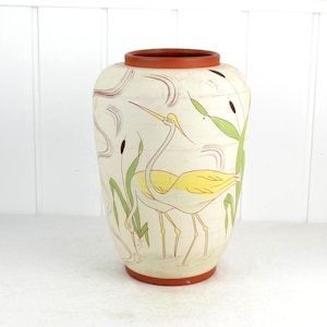 May include: A white ceramic vase with a yellow and green bird design. The vase has a rounded body and a brown rim.