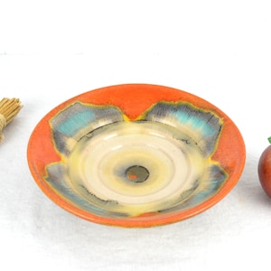 Könnte beinhalten: Eine Keramikschale mit einem weißen Zentrum und einem orangefarbenen, blauen und gelben Rand. Die Schale hat ein einzigartiges, wirbelndes Design.