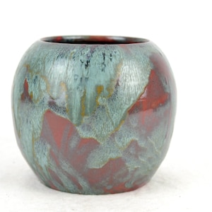 May include: A round ceramic vase with a blue-green and red glaze. The glaze has a mottled, textured appearance.