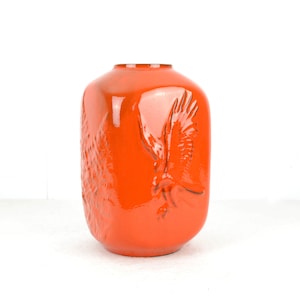 Könnte beinhalten: Orangefarbene Keramikvase mit einem Reliefdesign eines Vogels im Flug.