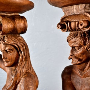 Puede incluir: Dos esculturas de madera talladas intrincadamente de figuras sosteniendo una plataforma circular. Las esculturas est&aacute;n hechas de madera marr&oacute;n oscura y presentan expresiones faciales detalladas y cabello elaborado.