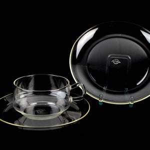 May include: A clear glass teacup and saucer set with a gold rim. The saucer is slightly larger than the teacup.