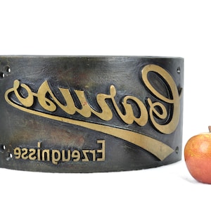 Könnte beinhalten: Ein vintage Metallschild mit dem Wort "Garwood" in goldenen Lettern geprägt. Das Schild ist gebogen und hat eine dunkelbraune Patina. Der Text "Erzeugnisse" ist ebenfalls auf dem Schild zu sehen.