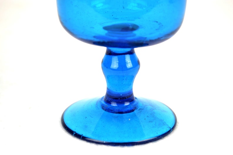 May include: A cobalt blue glass goblet with a wide bowl and a short stem. The goblet has a textured surface and a round base.