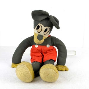 May include: A vintage plush toy of Mickey Mouse, with a grey body, red trousers, and black shoes. The toy has a black felt hat and large, white eyes.