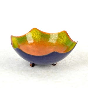 May include: A small, blue, ceramic bowl with a wavy rim. The bowl is decorated with a layered glaze of green, orange, and yellow.