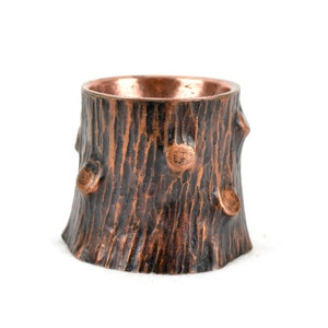 May include: A copper-colored metal planter shaped like a tree stump with a rough, textured surface.