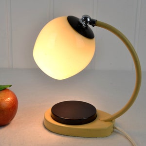 May include: A yellow and black vintage desk lamp with a white glass shade. The lamp has a curved arm and a round base.