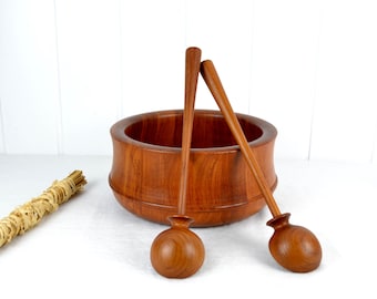 May include: A set of two wooden salad servers with rounded bowls and long handles, resting inside a large, round, wooden salad bowl.