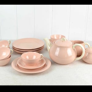 Op de afbeelding: Een roze theeservies met een theepot, suikerpot, roomkan, vier kopjes en vier schoteltjes. De set is gemaakt van keramiek en heeft een glanzende afwerking.