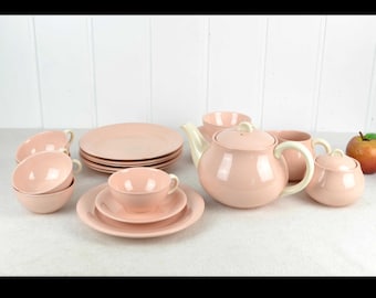 Op de afbeelding: Een roze theeservies met een theepot, suikerpot, roomkan, vier kopjes en vier schoteltjes. De set is gemaakt van keramiek en heeft een glanzende afwerking.