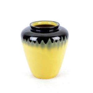 Può includere: Un vaso in ceramica giallo e nero con un design a festoni intorno al bordo. Il vaso è smaltato di colore giallo con una smaltatura nera e verde nella parte superiore.