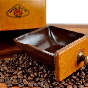 K&ouml;nnte beinhalten: Eine Kaffeem&uuml;hle aus Holz mit einer Schublade, die ge&ouml;ffnet ist und mit Kaffeebohnen gef&uuml;llt ist. Die Schublade hat einen Messingknopf. Die M&uuml;hle hat ein Etikett mit der Aufschrift "DREH-MEH".