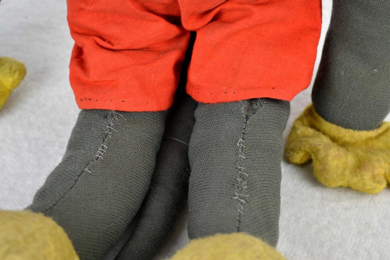 May include: Close-up of a vintage Mickey Mouse plush toy. The toy is wearing red shorts and has black felt legs with visible stitching. The toy's hands are yellow felt.