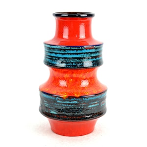 Könnte beinhalten: Eine Keramikvase mit leuchtend roter Grundfarbe, die zwei horizontale Bänder aus texturierter dunkelblauer und türkisfarbener Glasur aufweist. Die Vase hat eine mehrstufige, bauchige Silhouette mit einem schmalen Hals und einem ausgestellten Rand.