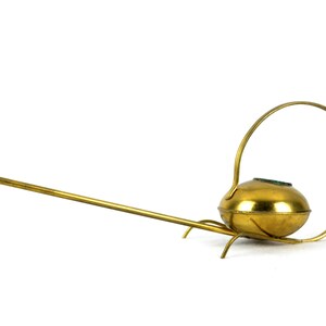 May include: A gold watering can with a long spout and a circular handle. The watering can has a round body and a small opening on the top.