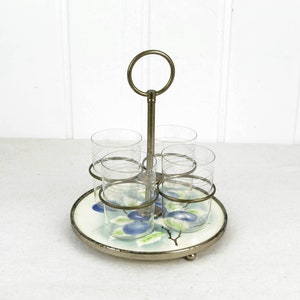 Può includere: Un porta bicchieri da shot vintage in vetro con un supporto in metallo e una base rotonda. La base è decorata con un motivo floreale blu e bianco. Il porta bicchieri ha quattro bicchieri da shot in vetro.