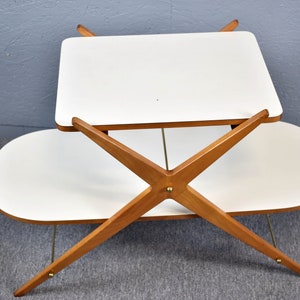 May include: A white two-tiered table with a wooden X-shaped base. The table has a rectangular top and an oval bottom shelf.