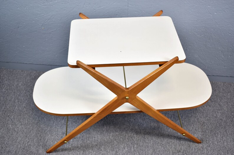 May include: A white two-tiered table with a wooden X-shaped base. The table has a rectangular top and an oval bottom shelf.