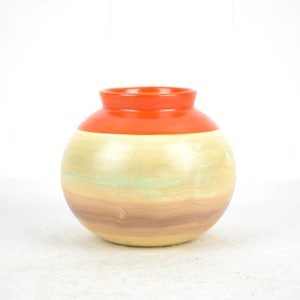 May include: A round ceramic vase with a layered design. The top layer is a bright orange, the middle layer is a light beige, and the bottom layer is a brown color.