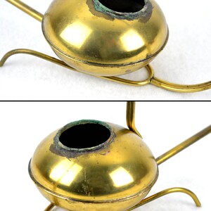 May include: A brass watering can with a round body and a long spout. The watering can is on a stand with three legs.