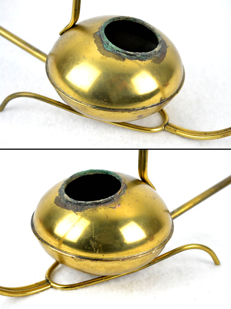 May include: A brass watering can with a round body and a long spout. The watering can is on a stand with three legs.