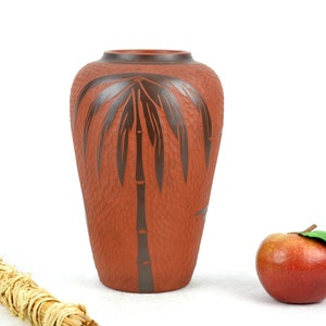 May include: A terracotta vase with a textured surface and a dark brown palm tree design.