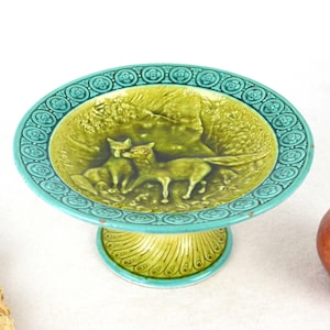 Könnte beinhalten: Eine Vintage-Tischschale in Türkis und Gelbgrün. Die Schale zeigt ein erhabenes Reliefdesign von zwei Pferden in einer Waldszene. Der Rand hat ein dekoratives Blumenmuster.